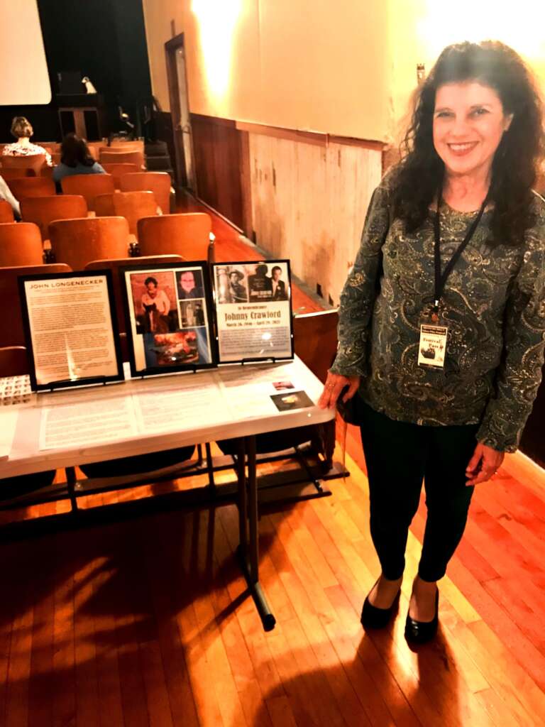 A woman inside a theatre standing next to a table with a row of framed photos.